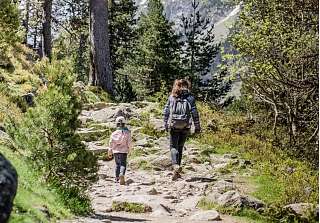 Mutter und Kind wandern Hand in Hand auf einem steinigen Pfad durch den herbstlichen Bergwald bei Arosa