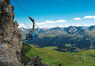 Téléphérique survolant les alpages verdoyants d’Arosa avec vue sur les Alpes suisses et la vallée.