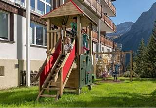 Des enfants jouent sur une aire de jeux en bois avec toboggan au Sunstar Hotel Arosa, en montagne, par beau temps.